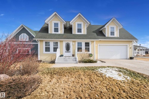 The property features a yellow exterior with white trim, a green shingled roof, and a prominent front door with an oval window - 17 Sunset Harbour, Rural Wetaskiwin County, AB - Outdoor With Facade