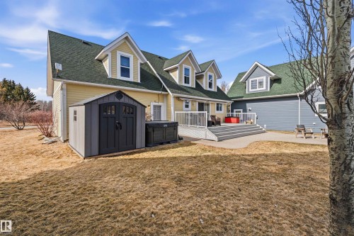 The property features a yellow exterior with a green roof, dormer windows, and a spacious deck - 17 Sunset Harbour, Rural Wetaskiwin County, AB - Outdoor With Deck Patio Veranda