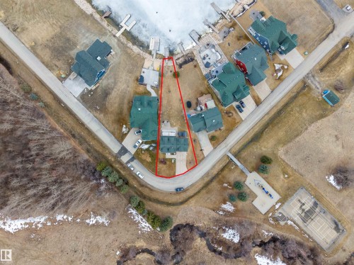 Aerial view of the property, indicated by the red outline, showcasing its position along a paved road and proximity to a body of water with docks - 17 Sunset Harbour, Rural Wetaskiwin County, AB - Other
