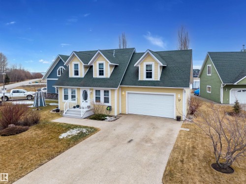 The property features a charming exterior with dormer windows, a front porch with white railings, and an attached garage with a white door - 17 Sunset Harbour, Rural Wetaskiwin County, AB - Outdoor With Facade