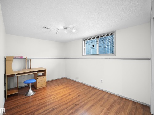The room features warm-toned hardwood flooring, white walls with a gray chair rail, and a window for natural light - 14523 32 Street, Edmonton, AB - Indoor Photo Showing Other Room