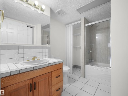 Bathroom featuring a wood vanity with a white tiled countertop and backsplash, a built-in sink, and a shower-over-bath with a glass enclosure - 14523 32 Street, Edmonton, AB - Indoor Photo Showing Bathroom