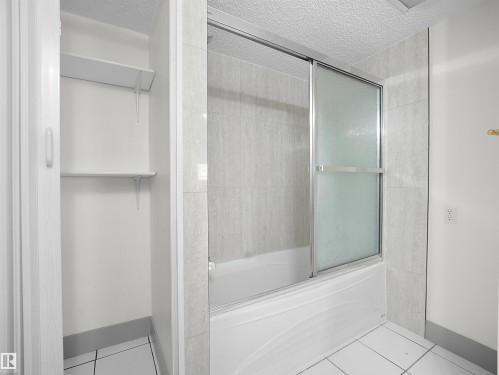 This bathroom features a shower and tub combination with sliding glass doors, white tile flooring, and a tiled shower surround - 14523 32 Street, Edmonton, AB - Indoor Photo Showing Bathroom