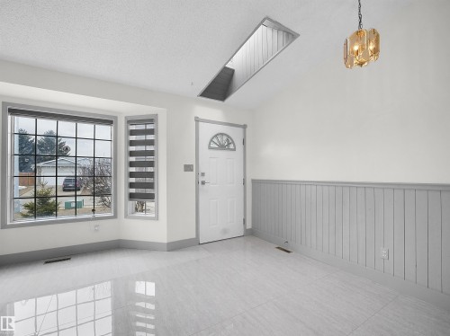 Entryway featuring a decorative front door, bay windows, sleek tile flooring, wainscoting, and a unique overhead light fixture - 14523 32 Street, Edmonton, AB - Indoor Photo Showing Other Room