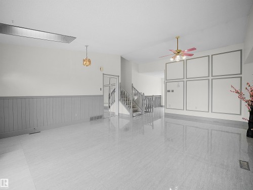 Spacious interior featuring light-colored tiled flooring, wainscoting, and a staircase with light-colored banisters - 14523 32 Street, Edmonton, AB - Indoor