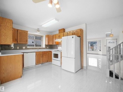 The kitchen features wood cabinetry, white appliances, and a tiled backsplash - 14523 32 Street, Edmonton, AB - Indoor Photo Showing Kitchen