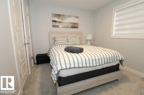 This room features light-colored carpeting, a window with horizontal blinds, and a light-toned bed frame with a headboard - 22140 81 Avenue, Edmonton, AB 