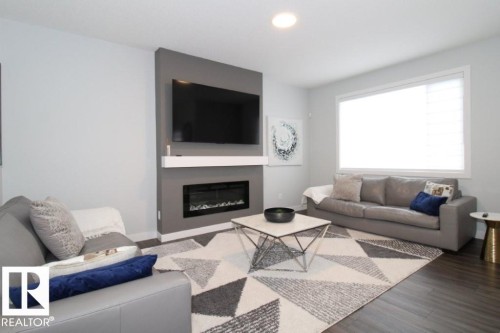 The living area features dark wood-style flooring, a recessed electric fireplace with a mantel, and a large window providing natural light - 22140 81 Avenue, Edmonton, AB 