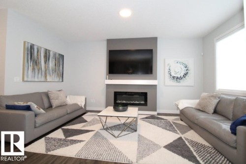 Living room featuring dark wood-style flooring, a large window, and a fireplace with a mantel - 22140 81 Avenue, Edmonton, AB 