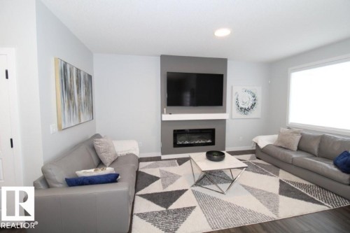 Living room featuring dark wood-style flooring, a geometric patterned area rug, and a modern fireplace with a white mantel and gray accent wall - 22140 81 Avenue, Edmonton, AB 