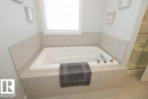 Bathroom featuring a built-in bathtub with light-colored tile surround, a window with blinds, and light-colored walls - 22140 81 Avenue, Edmonton, AB 