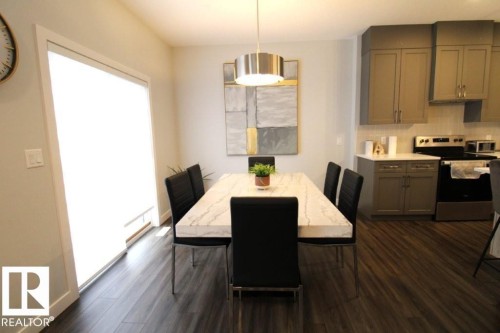 The dining area features a contemporary chandelier, a large window providing natural light, and dark wood-style flooring - 22140 81 Avenue, Edmonton, AB 