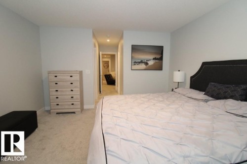This bedroom features light-colored walls and carpeting, a dark upholstered headboard with stud detailing, and a hallway view with recessed lighting - 22140 81 Avenue, Edmonton, AB 