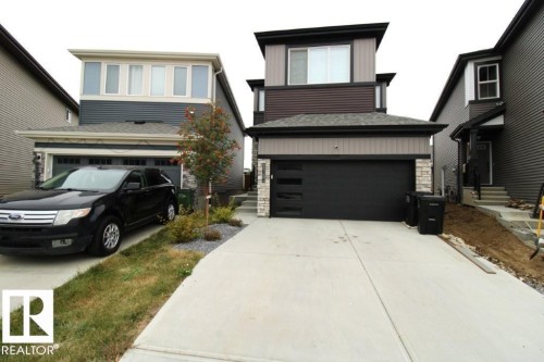 The property features a concrete driveway and a modern black garage door with frosted window panels - 22140 81 Avenue, Edmonton, AB 