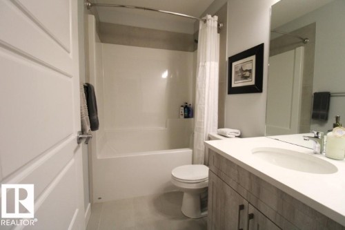 The bathroom features a vanity with a white countertop and a rectangular sink, a toilet, and a combination bathtub and shower with a shower curtain - 22140 81 Avenue, Edmonton, AB 
