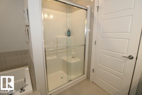 The bathroom features a built-in bathtub with chrome fixtures, a shower with a sliding glass door, and tiled walls - 22140 81 Avenue, Edmonton, AB 