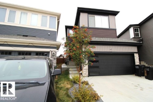 The property features a dark-colored garage door with horizontal window accents, a paved driveway, and stone column detailing on the facade - 22140 81 Avenue, Edmonton, AB 