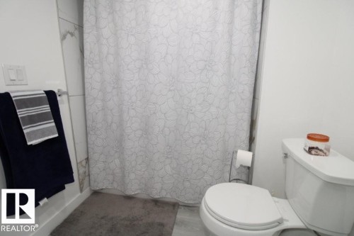 Bathroom featuring a toilet, a shower with a patterned curtain, and tiled walls - 22140 81 Avenue, Edmonton, AB 