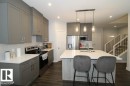 The kitchen features grey cabinetry, stainless steel appliances, a white tile backsplash, and a large island with a white countertop and seating - 22140 81 Avenue, Edmonton, AB 