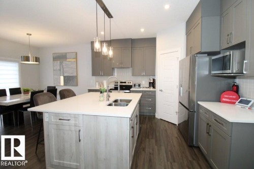 The kitchen features an island with a double sink, light grey cabinetry, and stainless steel appliances including a refrigerator and microwave - 22140 81 Avenue, Edmonton, AB 