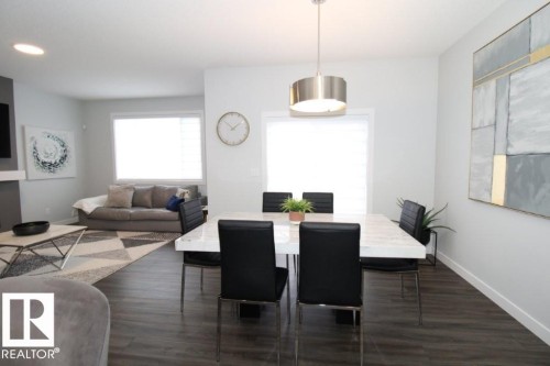 This property features an open living and dining area with dark wood flooring, light-colored walls, and large windows providing natural light - 22140 81 Avenue, Edmonton, AB 