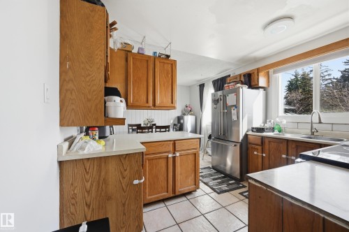 The kitchen features wood cabinetry, light-colored countertops, a stainless steel refrigerator, and a window with an outdoor view - 9031 133 Avenue, Edmonton, AB - Indoor Photo Showing Kitchen