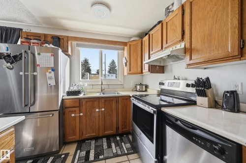 The kitchen features wood cabinetry, a stainless steel refrigerator, an electric range, and a window above the sink - 9031 133 Avenue, Edmonton, AB - Indoor Photo Showing Kitchen With Double Sink