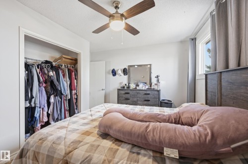 This bedroom features a ceiling fan with integrated lighting, a window with curtains, and a built-in closet with a hanging rod - 9031 133 Avenue, Edmonton, AB - Indoor Photo Showing Bedroom