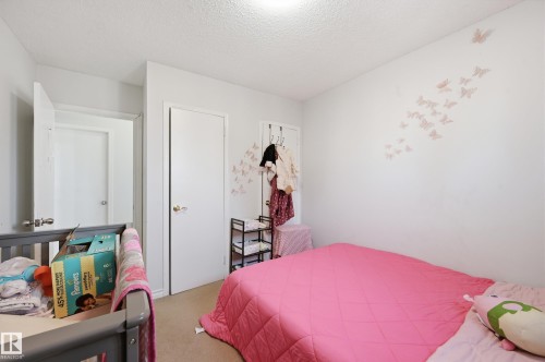 This room features light-colored walls and carpeted flooring, with a solid door providing access to another area of the property - 9031 133 Avenue, Edmonton, AB - Indoor Photo Showing Bedroom