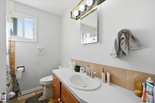 Bathroom featuring a white vanity with a single sink, a wall-mounted mirror, and a window providing natural light - 9031 133 Avenue, Edmonton, AB - Indoor Photo Showing Bathroom