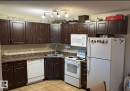 Well-appointed kitchen featuring dark wood cabinetry, a double basin stainless steel sink, and white appliances including a refrigerator, stove, microwave, and dishwasher - 408 309 Clareview Station Drive Nw, Edmonton, AB  - Indoor Photo Showing Kitchen 