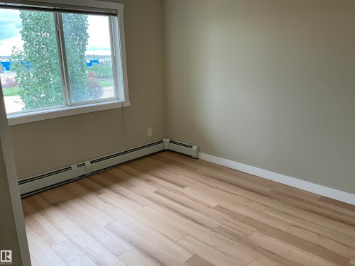 Interior space featuring a window with white trim, light wood-finish flooring, baseboard heating, and neutral wall paint - 408 309 Clareview Station Drive Nw, Edmonton, AB 
