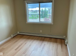 Light-colored wood-finish flooring, neutral wall paint, and a large window with blinds - 