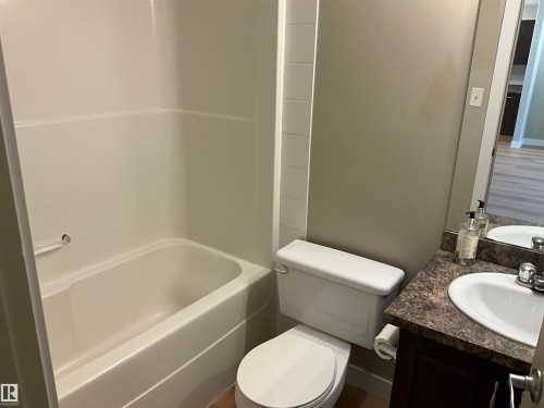 Bathroom featuring a white bathtub and shower surround, a white toilet, and a vanity with a dark countertop and integrated sink - 408 309 Clareview Station Drive Nw, Edmonton, AB 