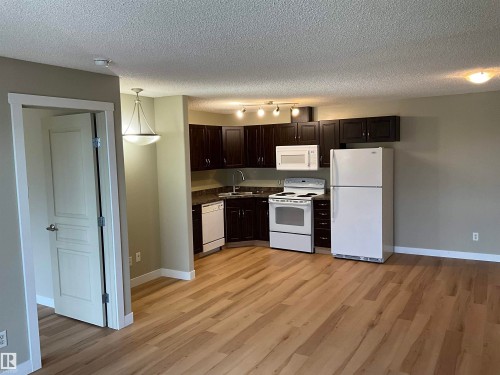 Open-concept kitchen and living area featuring wood-finish flooring, dark wood cabinetry, white appliances, and a tiled backsplash - 408 309 Clareview Station Drive Nw, Edmonton, AB 