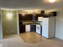 Compact kitchen featuring dark wood cabinetry, a double-basin sink, and white appliances including a refrigerator, range, microwave, and dishwasher - 408 309 Clareview Station Drive Nw, Edmonton, AB  - Indoor Photo Showing Kitchen 