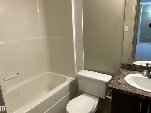 Bathroom featuring a built-in bathtub with shower surround, a toilet, and a vanity with an integrated sink and laminate countertop - 408 309 Clareview Station Drive Nw, Edmonton, AB - Indoor Photo Showing Bathroom