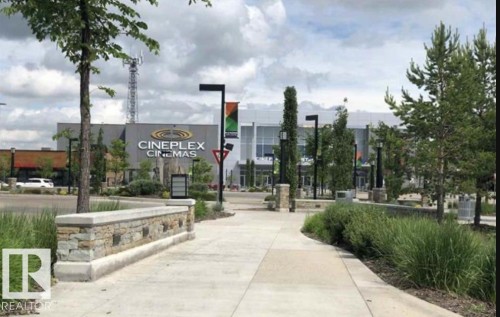 View of the Cineplex Cinemas building with a paved walkway and landscaped areas featuring trees and shrubs - 408 309 Clareview Station Drive Nw, Edmonton, AB - Outdoor With View