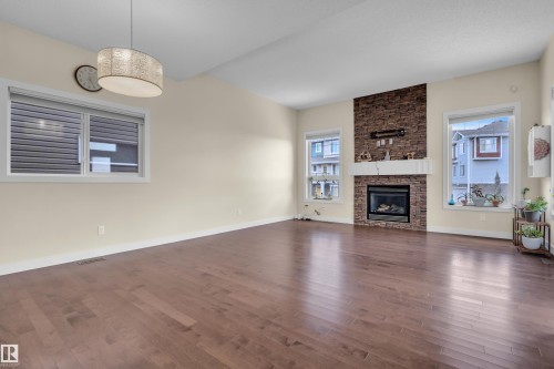 Living area featuring hardwood flooring, a vaulted ceiling, and a prominent fireplace with a stone surround - 3071 Carpenter Landing Landing, Edmonton, AB - Indoor Photo Showing Living Room With Fireplace