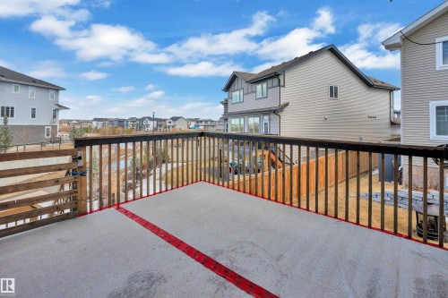 The property features a concrete patio with a wooden railing and gate, offering views of surrounding residences and a distant pond - 3071 Carpenter Landing Landing, Edmonton, AB - Outdoor With Exterior