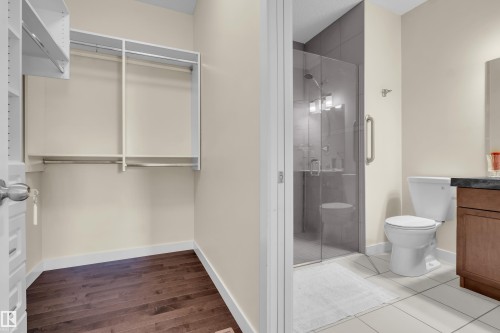 This space features a well-organized closet with shelving and hanging rods, alongside a bathroom with a glass-enclosed shower, toilet, and a vanity with a dark countertop - 3071 Carpenter Landing Landing, Edmonton, AB - Indoor Photo Showing Bathroom
