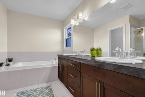 Bathroom featuring a built-in bathtub, a window, and a vanity with two sinks and a large mirror - 3071 Carpenter Landing Landing, Edmonton, AB - Indoor Photo Showing Bathroom