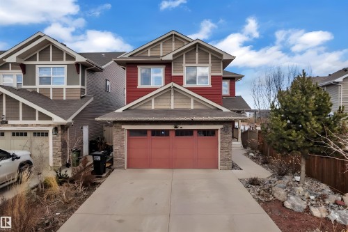 The property features a two-story design with red siding and light brown accents, a two-car garage with a red door, and a concrete driveway - 3071 Carpenter Landing Landing, Edmonton, AB - Outdoor With Facade