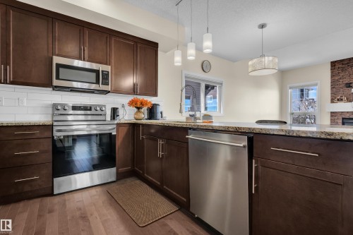 The kitchen features dark wood cabinetry, stainless steel appliances, and granite countertops - 3071 Carpenter Landing Landing, Edmonton, AB - Indoor Photo Showing Kitchen With Upgraded Kitchen