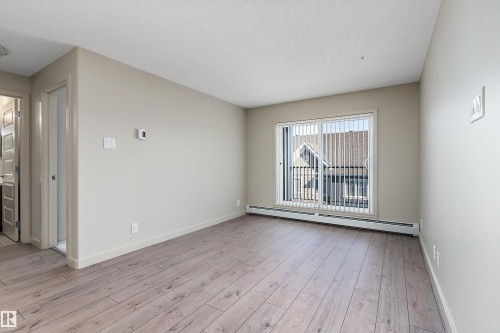 The room features light-colored laminate flooring, neutral wall paint, and a sliding glass door with vertical blinds - 309 4008 Savaryn Drive, Edmonton, AB - Indoor Photo Showing Other Room