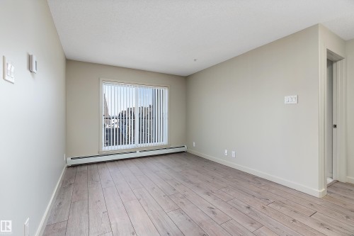 This room features light-colored plank flooring, neutral wall paint, and a large window with vertical blinds - 309 4008 Savaryn Drive, Edmonton, AB - Indoor Photo Showing Other Room