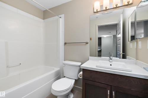 The bathroom features a white bathtub and shower unit, a toilet, and a vanity with a white countertop and a rectangular sink - 309 4008 Savaryn Drive, Edmonton, AB - Indoor Photo Showing Bathroom