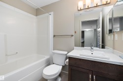 The bathroom features a white bathtub and shower unit, a toilet, and a vanity with a white countertop and a rectangular sink - 