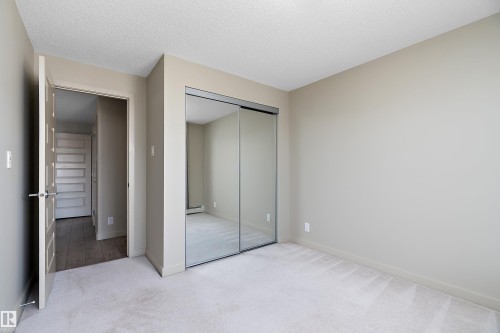 This room features neutral-toned walls, light-colored carpeting, and mirrored sliding closet doors - 309 4008 Savaryn Drive, Edmonton, AB - Indoor Photo Showing Other Room