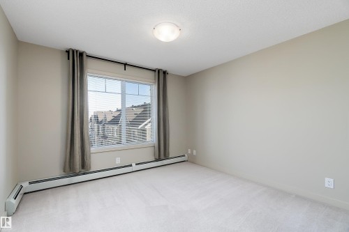 This room features a window with blinds and drapes, light-colored carpeting, and neutral-toned walls - 309 4008 Savaryn Drive, Edmonton, AB - Indoor Photo Showing Other Room